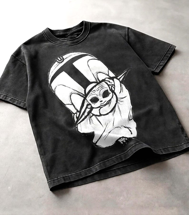 Peut inclure: T-shirt gris fonc&eacute; avec un motif blanc repr&eacute;sentant un personnage de science-fiction. Le motif est une illustration stylis&eacute;e d'une petite cr&eacute;ature extraterrestre. Le t-shirt a un col rond et des manches courtes.