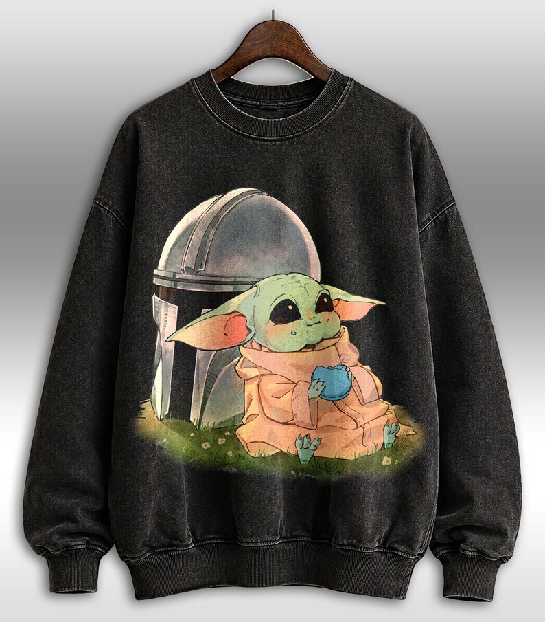 May include: Black crew neck sweatshirt with a graphic of a green alien character holding a blue sphere, with a helmet behind. The alien is wearing a tan robe and sitting on grass. The sweatshirt has a faded, vintage appearance.