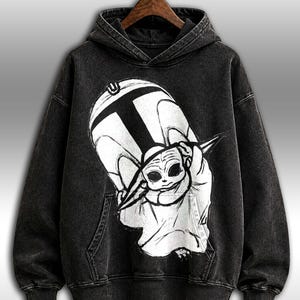 Peut inclure: Sweat-shirt &agrave; capuche noir avec un grand motif en noir et blanc d'un personnage de dessin anim&eacute;. Le sweat-shirt a une poche kangourou et une capuche &agrave; cordon. Le motif repr&eacute;sente un personnage avec de grands yeux et une t&ecirc;te pointue.