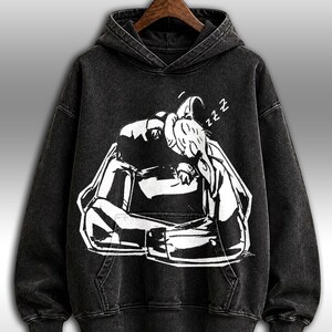 K&ouml;nnte beinhalten: Schwarzer Kapuzenpullover mit einer wei&szlig;en Grafik einer schlafenden Person, mit dem Wort "zzz" &uuml;ber dem Kopf. Der Pullover hat eine Vordertasche und eine Kapuze mit Kordelzug. Der Stoff hat einen verwaschenen Vintage-Look.