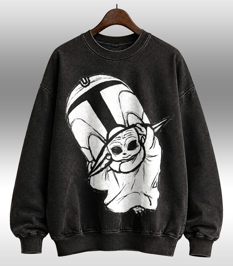 Peut inclure: Sweat-shirt noir &agrave; col rond avec un motif graphique en noir et blanc d'un personnage de dessin anim&eacute;. Le motif comprend un grand "T" et une repr&eacute;sentation stylis&eacute;e d'un personnage avec de grands yeux. Le sweat-shirt a des poignets et un ourlet c&ocirc;tel&eacute;s.