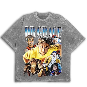 May include: Grey acid wash t-shirt with a collage of images and the text "DR GRACE Rocky" in blue and white. The design includes a central portrait of a man in a yellow shirt, surrounded by other portraits.