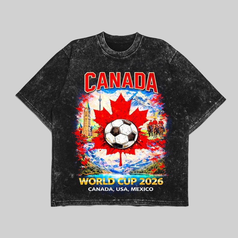 May include: Black t-shirt with a graphic featuring a soccer ball on a red maple leaf, the word "CANADA" in red, and "WORLD CUP 2026" with "CANADA, USA, MEXICO" below. The design includes a scenic background.