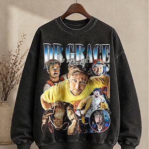 May include: Black vintage-style sweatshirt with a graphic of a person and the text "DR GRACE Rocky" in blue and white. The graphic includes multiple images of the person. The sweatshirt has a crew neck and long sleeves. The garment has a faded appearance.