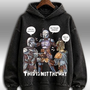 K&ouml;nnte beinhalten: Schwarzer Kapuzenpullover mit einer Grafik von drei gepanzerten Figuren und Sprechblasen. Der Text "THIS IS NOT THE WAY" ist darunter gedruckt. Die Sprechblasen sagen "Give me your armor!", "Hey! Enough! Extremist!" und "Shut up! Kid!"