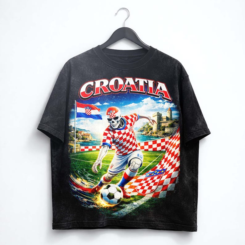May include: Black t-shirt featuring a soccer-playing skeleton in a Croatian team uniform. The design includes the word "CROATIA" in red and white, a Croatian flag, and a castle in the background. The shirt is hanging on a black hanger.