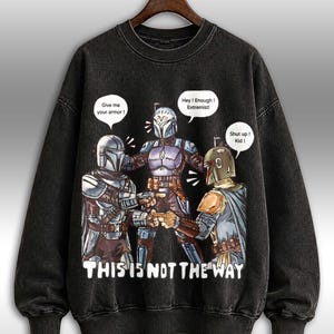 K&ouml;nnte beinhalten: Schwarzes Sweatshirt mit Rundhalsausschnitt und einer Grafik von drei Charakteren in R&uuml;stungen mit Sprechblasen. Der Text "THIS IS NOT THE WAY" ist unter den Charakteren aufgedruckt. Die Sprechblasen sagen "Give me your armor!", "Hey! Enough! Extremist!" und "Shut up! Kid!"