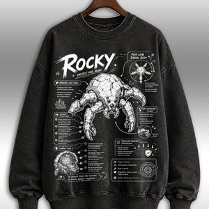 May include: Dark grey crew neck sweatshirt featuring a detailed crab-like creature illustration with scientific diagrams. The word "Rocky" is above the creature. Text includes "Project Hail Mary".