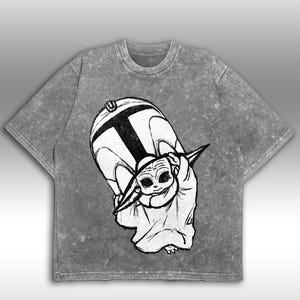 Peut inclure: T-shirt gris d&eacute;lav&eacute; &agrave; l'acide avec une illustration en noir et blanc d'un personnage d'une franchise de science-fiction populaire. Le graphisme repr&eacute;sente un grand casque et une petite cr&eacute;ature extraterrestre. Le t-shirt a un col rond et des manches courtes.