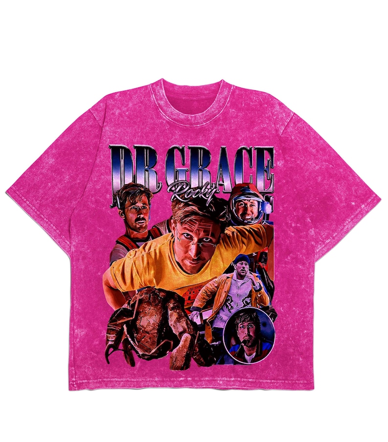 May include: A pink acid wash t-shirt with a graphic featuring the text "DR GRACE Rocky" and a collage of images. The images show a person in different outfits. The t-shirt has a crew neck and short sleeves.