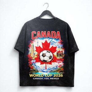 May include: Black t-shirt featuring a soccer ball on a red maple leaf, with the word "CANADA" in red and white. The shirt also displays "WORLD CUP 2026" and the host countries: Canada, USA, and Mexico.