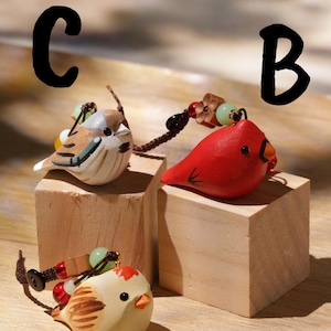 May include: Three bird-shaped charms labeled A, B, and C. Charm A is a cream bird with brown wings. Charm B is a bright red bird with a black face patch. Charm C is a brown and white sparrow-like bird. Each charm features colorful beads.