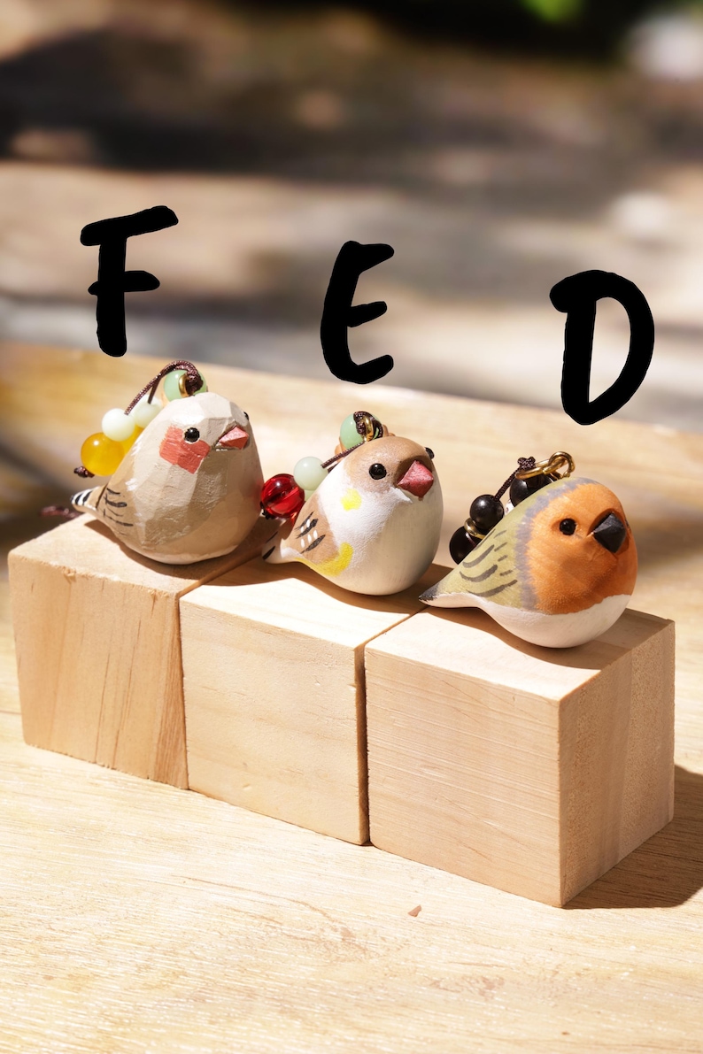 May include: Three small carved bird figurines labeled F, E, and D. The first is beige with red cheek patches, the second is white with yellow and brown accents, and the third is orange and brown. Each bird features a small beaded charm attachment.