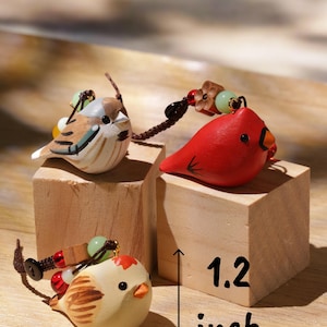 May include: Three small bird-shaped charms with brown, red, and cream painted details, each featuring a dark cord and decorative beads. The charms are displayed on wooden blocks with text indicating a height of 1.2 inches and width of 1.8 inches.