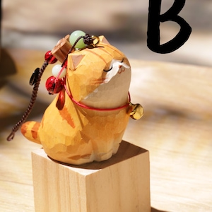 May include: A carved wooden cat figurine with orange and white coloring, sitting on a small wooden block. The cat has a red collar and a small gold bell. A black "B" is in the background.