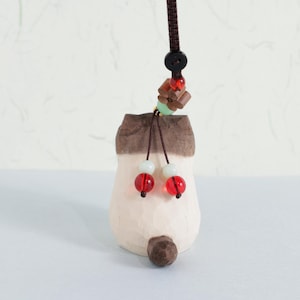 May include: A carved wooden ornament in the shape of a stylized mushroom. The mushroom is off-white with a brown cap and base. It has a brown cord with decorative beads in red, green, and white. The ornament is designed for hanging.