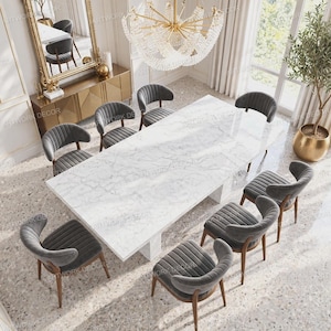 Op de afbeelding: Een rechthoekige eettafel van wit marmer met grijze aders, gecombineerd met acht donkergrijze gestoffeerde stoelen met verticale kanaalstiksels en houten poten, opgesteld in een formele eetkamer met een grote kristallen kroonluchter.