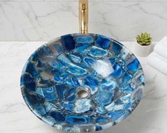 May include: A round, blue and white agate stone vessel sink with a gold faucet. The sink is made of polished stone and has a unique, mosaic-like pattern. The sink is a decorative bathroom fixture.