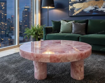 May include: A round coffee table made of pink stone with three cylindrical legs. The table is set on a gray rug in a living room with a green sofa and a large window overlooking a city.