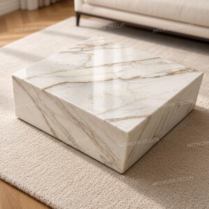 Puede incluir: Una mesa de centro cuadrada con una superficie de mármol blanco pulido con vetas grises y doradas prominentes. La mesa tiene una construcción sólida en forma de bloque con bordes limpios y afilados y un acabado liso y reflectante que resalta el patrón.