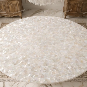 May include: A round table top featuring a mosaic surface composed of small, iridescent white mother-of-pearl tiles arranged in a concentric circular pattern. The tiles exhibit varying shades of cream, off-white, and pearlescent tones.