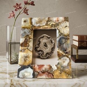 May include: A rectangular picture frame constructed from various polished agate slices in shades of beige, brown, gray, and white. The frame features a central opening displaying a single, circular, banded agate stone with a dark, crystalline center.