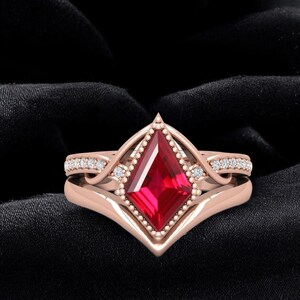 May include: A rose gold ring set with a striking, square-cut, red gemstone. The ring is embellished with small diamonds and a beaded edge. The set is displayed against a black backdrop.