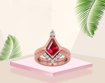 May include: Rose gold ring set featuring a central kite-shaped ruby gemstone. The ring is accented with small, round diamonds and intricate detailing. The set includes a matching band, creating a cohesive and elegant look.
