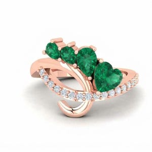 Puede incluir: Un anillo de oro rosa con una banda curva adornada con una hilera de pequeñas piedras claras. La parte superior muestra cuatro piedras preciosas verdes vibrantes de diversas formas, incluyendo cortes de pera y corazón.