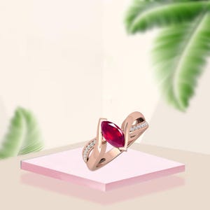 Peut inclure: Une bague en or rose ornée d'un rubis de forme marquise. La bague présente un design de bande torsadée avec de petits diamants étincelants sertis le long de la bande. Le rubis est d'un rouge profond, et la bague est présentée sur une surface rose.