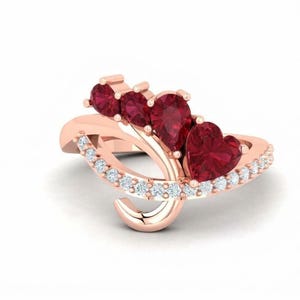 Puede incluir: Un anillo de oro rosa con una banda curva engastada con pequeñas piedras claras. La parte superior del anillo muestra un grupo de cuatro piedras preciosas de color rojo intenso, incluyendo dos redondas, una en forma de pera y una en forma de corazón.