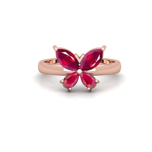 Può includere: Un anello in oro rosa con un elemento centrale a forma di farfalla composto da quattro pietre preziose rosso scuro con taglio a marquise e a goccia. Il gambo dell'anello è liscio e lucido, con le gemme fissate al centro della parte superiore.