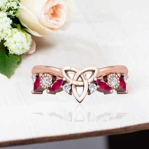 May include: Rose gold ring with a Celtic knot design, marquise-cut ruby gemstones, and round white diamonds. The ring's intricate design is ideal for special occasions. The gemstones are set in a symmetrical pattern, creating a balanced aesthetic.