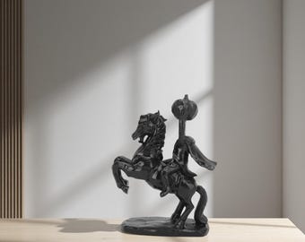 Könnte beinhalten: Eine schwarze Skulptur eines sich aufbäumenden Pferdes, geritten von einer kopflosen Figur, die einen Kürbis hält. Die Skulptur steht auf einer Holzoberfläche. Die Statue des kopflosen Reiters ist ein dekoratives Objekt.