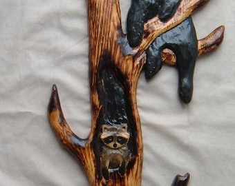 May include: A wooden carving of a tree with two black bears and a raccoon. The bears are climbing the tree and the raccoon is in the hollow of the tree. The carving is painted brown and black.