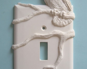 May include: White ceramic light switch cover with an owl perched on a branch. The owl and branch are sculpted in 3D.