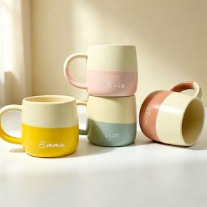 Peut inclure: Quatre tasses en céramique avec une partie supérieure crème mouchetée et une base unie. Une tasse est jaune avec le prénom Emma, une rose avec Olivia, une bleu sarcelle avec Liam et une terre cuite avec le prénom Olivia écrit en blanc.