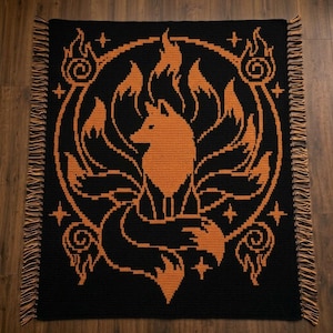 May include: A rectangular crochet blanket featuring a black background with a large orange graphic of a multi-tailed fox centered within a circular frame. The design includes flame-like motifs and small four-pointed stars, finished with fringe.