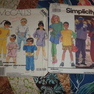May include: Two sewing pattern envelopes. The McCall's pattern envelope shows a group of children wearing colorful clothing. The Simplicity pattern envelope shows a group of children wearing casual clothing. Both envelopes have the pattern numbers printed on the front.