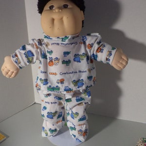 May include: A Cabbage Patch Kid doll wearing a white and blue pajamas with a construction theme. The pajamas have a pattern of trucks, construction signs, and the words "Construction Ahead" and "Work Zone".
