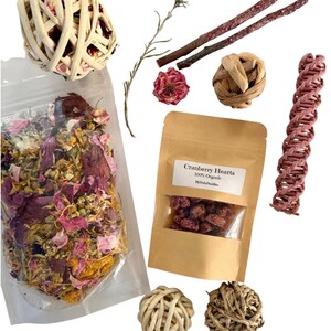 May include: An assortment of small pet supplies, including a woven ball, a bag of dried flowers, a bag of cranberry hearts, and several chew toys. The cranberry hearts bag has a label that reads "Cranberry Hearts 100% Organic".