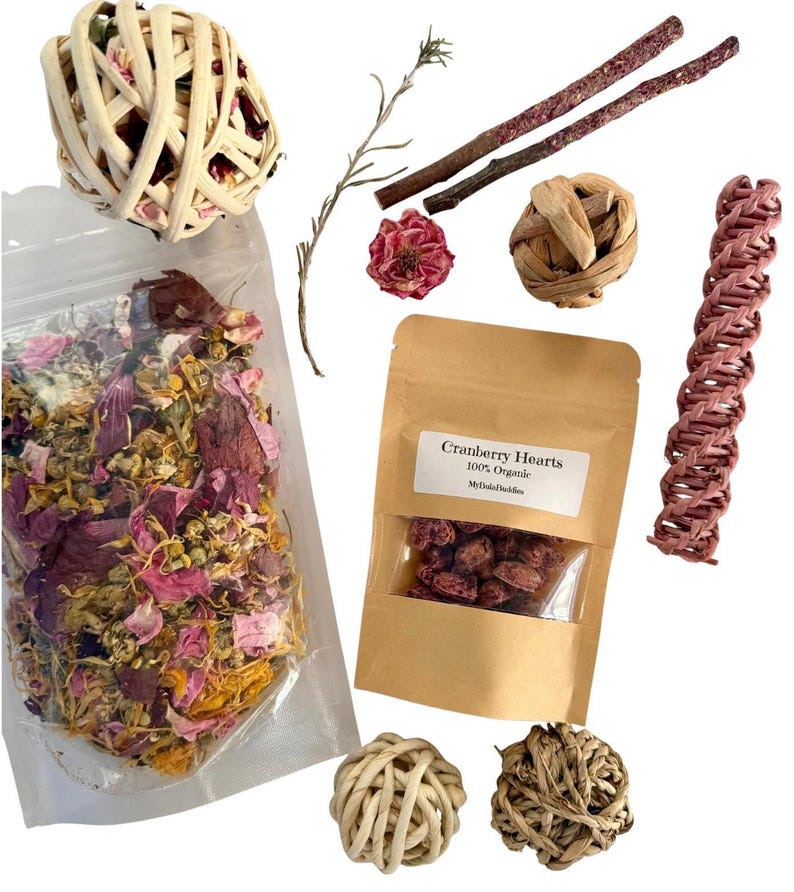 May include: An assortment of small pet supplies, including a woven ball, a bag of dried flowers, a bag of cranberry hearts, and several chew toys. The cranberry hearts bag has a label that reads "Cranberry Hearts 100% Organic".