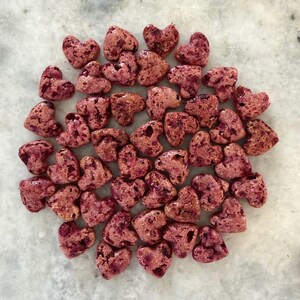 May include: A collection of heart-shaped candies in varying shades of pink and red, arranged on a light-colored surface. The candies have a textured appearance, suggesting a crunchy or crystallized exterior. The overall aesthetic is sweet and romantic.