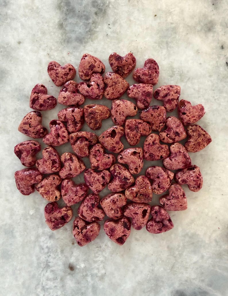 May include: A collection of heart-shaped candies in varying shades of pink and red, arranged on a light-colored surface. The candies have a textured appearance, suggesting a crunchy or crystallized exterior. The overall aesthetic is sweet and romantic.