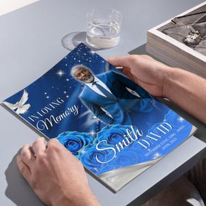 K&ouml;nnte beinhalten: Eine Gedenkbrosch&uuml;re mit blauem und wei&szlig;em Design. Das Cover zeigt ein Portr&auml;t eines Mannes in einem blauen Anzug, blaue Rosen und den Text "In Loving Memory" und "David Smith". Die Brosch&uuml;re wird von zwei H&auml;nden offen gehalten.