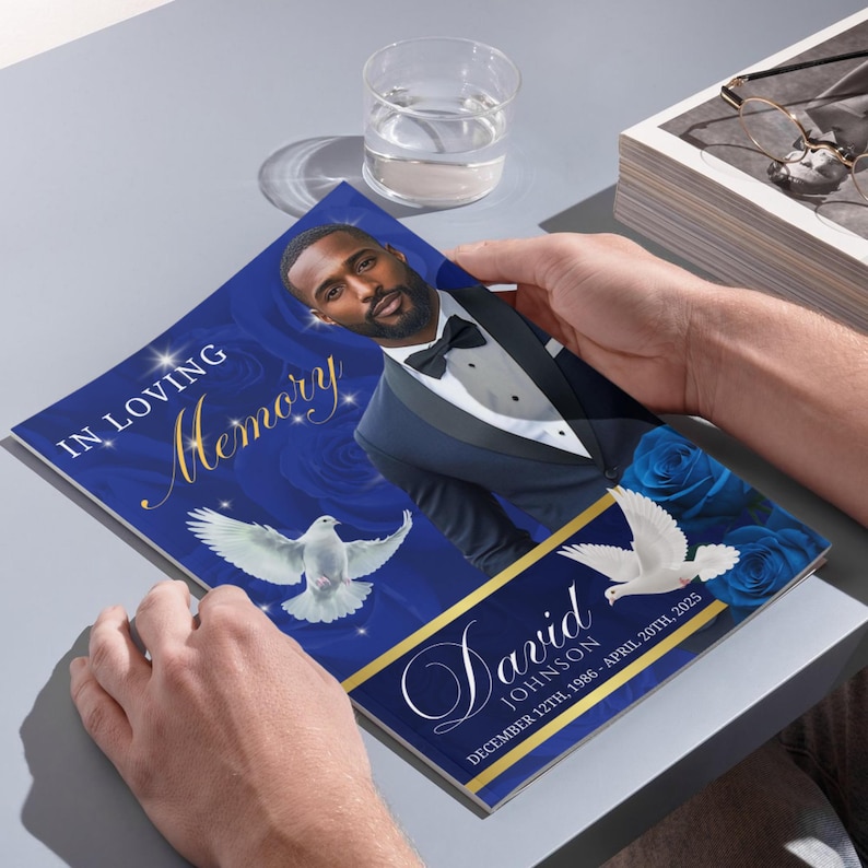 May include: A memorial card with a portrait of a man in a tuxedo, the words "In Loving Memory" and the name "David Johnson" are displayed on a blue background with white doves and blue roses. The card also includes the dates "December 12th, 1986 - April 20th, 2025."