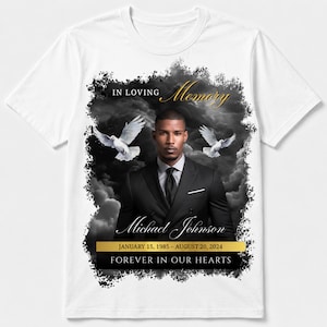 May include: A white t-shirt featuring a memorial graphic with a man in a black suit, two white doves, and dark clouds. Text reads: IN LOVING Memory, Michael Johnson, JANUARY 15, 1985 - AUGUST 20, 2024, and FOREVER IN OUR HEARTS in gold and white.