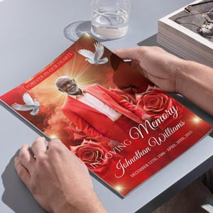 May include: A memorial booklet with a red cover featuring a portrait of a man in a red suit, surrounded by roses and doves. The text reads "Forever in Our Hearts" and "In Loving Memory Johnathan Williams, December 12th, 1986 - April 20th, 2025."