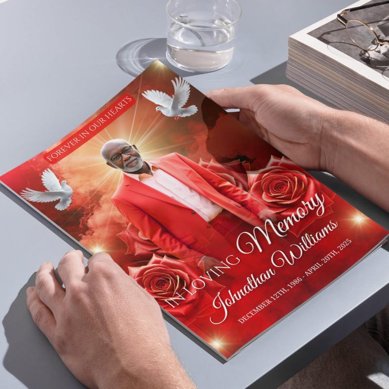May include: A memorial booklet with a red cover featuring a portrait of a man in a red suit, surrounded by roses and doves. The text reads "Forever in Our Hearts" and "In Loving Memory Johnathan Williams, December 12th, 1986 - April 20th, 2025."