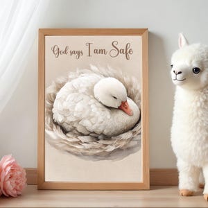 May include: A framed print featuring a watercolor illustration of a sleeping white swan nestled in a feathery nest. The text "God says I am Safe" is written above the swan. A plush llama toy is to the right.